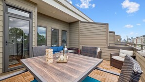 An outdoor patio with a wooden table, wicker furniture, and a view of the city skyline. - Cozy 3-Story Townhome w/ Rooftop & Skyline Views! (Nashville)