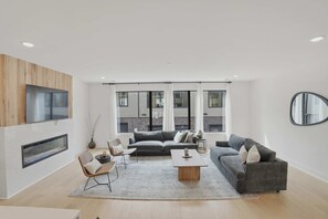 Ein modernes Wohnzimmer mit Kamin, zwei Sofas, einem Couchtisch und großen Fenstern.