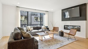 A modern living room with a sofa, coffee table, and a flat-screen TV mounted on the wall. - Luxury retreat with exclusive rooftop hot tub (Nashville)