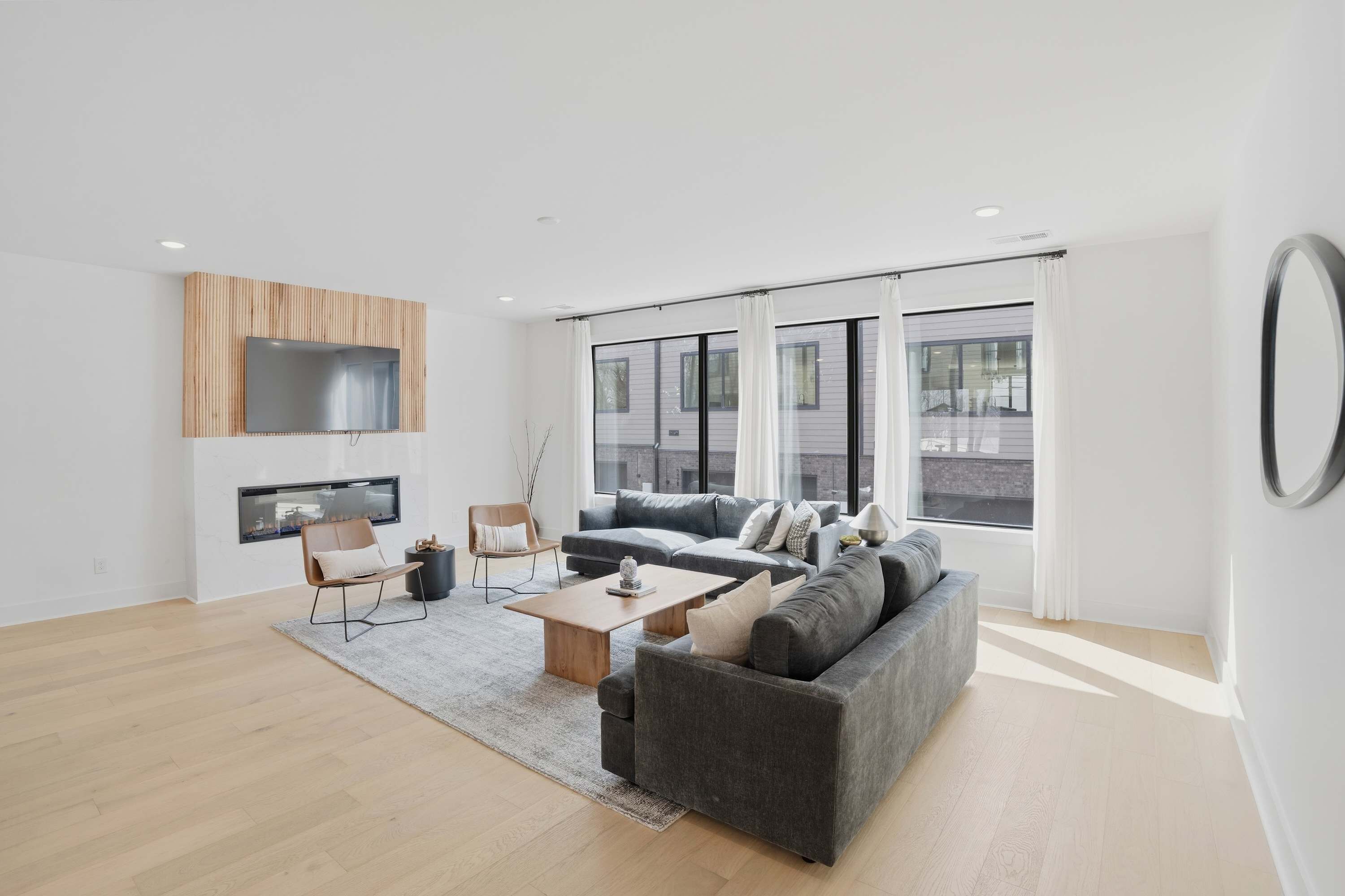 A modern living room with a grey sofa, wooden coffee table, and a TV mounted on a wooden panel.