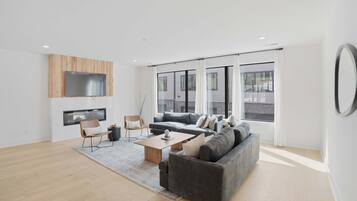 A modern living room with a grey sofa, wooden coffee table, and a TV mounted on a wooden panel.