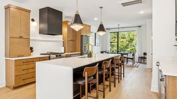 A modern kitchen with wooden cabinets, a central island with bar stools, pendant lighting, and a large window providing natural light. - Luxury retreat with exclusive rooftop hot tub (Nashville)