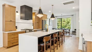 A modern kitchen with wooden cabinets, a central island with bar stools, pendant lighting, and a large window providing natural light.
