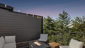 An outdoor patio with a built-in fire feature, wicker furniture, and string lights. - Luxury retreat with exclusive rooftop hot tub (Nashville)