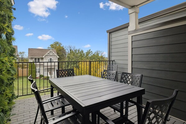 Een terras met een tafel en stoelen, een hekwerk en een uitzicht op een huis op de achtergrond.
