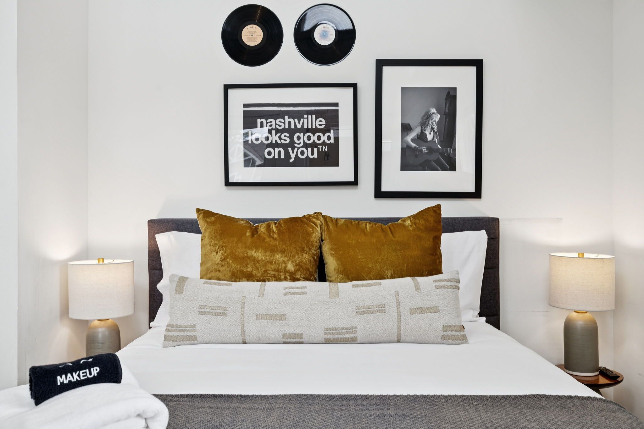 Ein ordentlich bezogenes Bett mit zwei Kissen, ein gerahmter Spruch an der Wand und zwei Schallplatten.