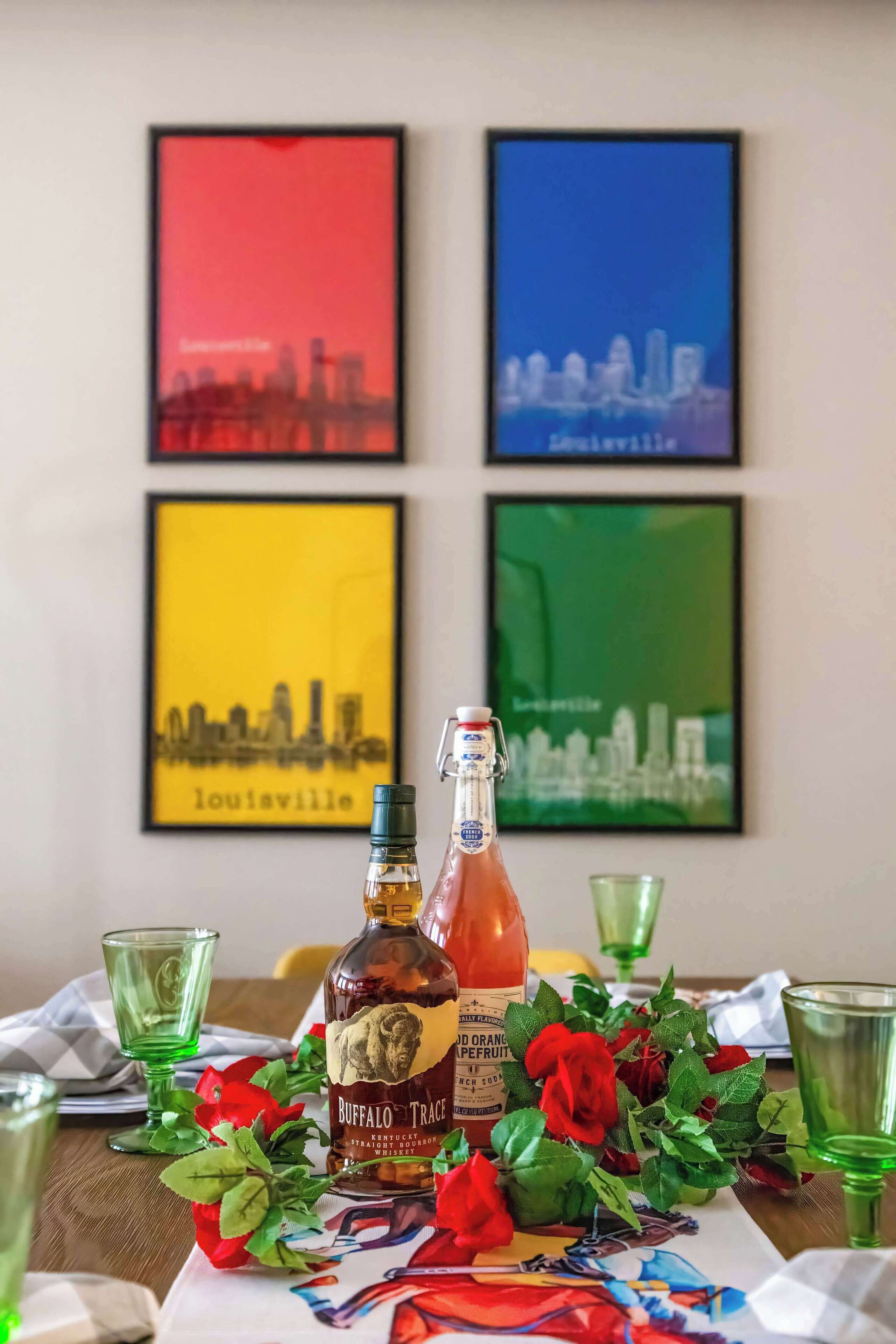 Une table avec deux bouteilles de whisky, des verres verts et des roses rouges.