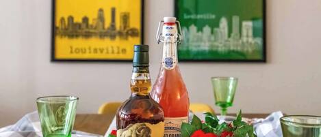 Une table avec deux bouteilles de whisky, des verres verts et des roses rouges.