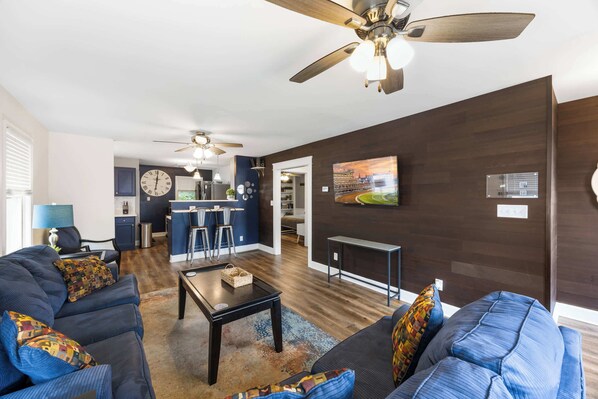 Een moderne woonkamer met donker houten vloeren, een grote zithoek, een salontafel, en een eethoek met barstoelen.