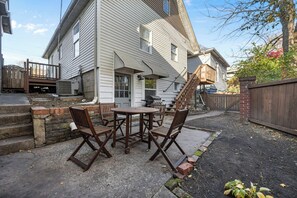 Een achtertuin met terras, met een ronde tafel en vier stoelen.