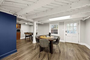 Een kamer met een ronde tafel, twee stoelen, een tafelvoetbaltafel en een deur met een glas-in-loodraam.