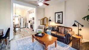 A living room with a brown leather sofa, a wooden coffee table, and a chandelier. - Modern apartment near Nulu and other attractions! (Louisville)
