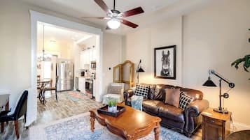 A living room with a brown leather sofa, a wooden coffee table, and a chandelier.