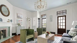 Una sala de estar con chimenea, sillones verdes, una mesa de centro y un tapete estampado.