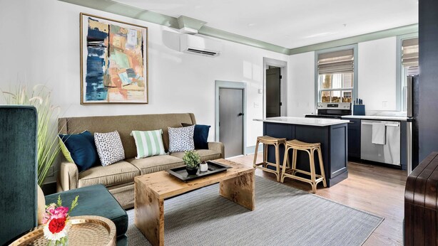 A modern living room with a sofa, coffee table, and a kitchen area with a bar stool. - Cozy + Spacious 2bd King Suites w. Gym & Parking! (Charleston)