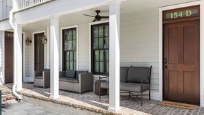 A porch with two wicker sofas, a ceiling fan, and a wooden door with a number sign. - Cozy + Spacious 2bd King Suites w. Gym & Parking! (Charleston)