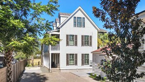 A two-story white house with a balcony, a paved driveway, and surrounding trees. - Cozy + Spacious 2bd King Suites w. Gym & Parking! (Charleston)