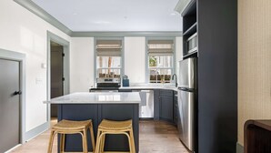A modern kitchen with a large island, dark cabinetry, and a view of the backyard. - Cozy + Spacious 2bd King Suites w. Gym & Parking! (Charleston)