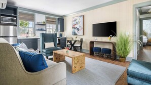 Una sala de estar moderna con un sofá, una mesa de centro y un televisor. Hay una zona de cocina con microondas y armarios.