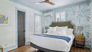 Un dormitorio con una cama grande, un ventilador de techo y una ventana con contraventanas.
