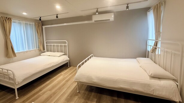 A room with two single beds, a window with curtains, an air conditioning unit, and a ceiling light. - 3-101: Newly built Apt, 2 min sta., Near Skytree & Asakusa (Sumida City)