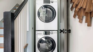 Een wasserette met twee gestapelde wasmachines, houten wanddecoratie en een trap met zwarte leuningen.
