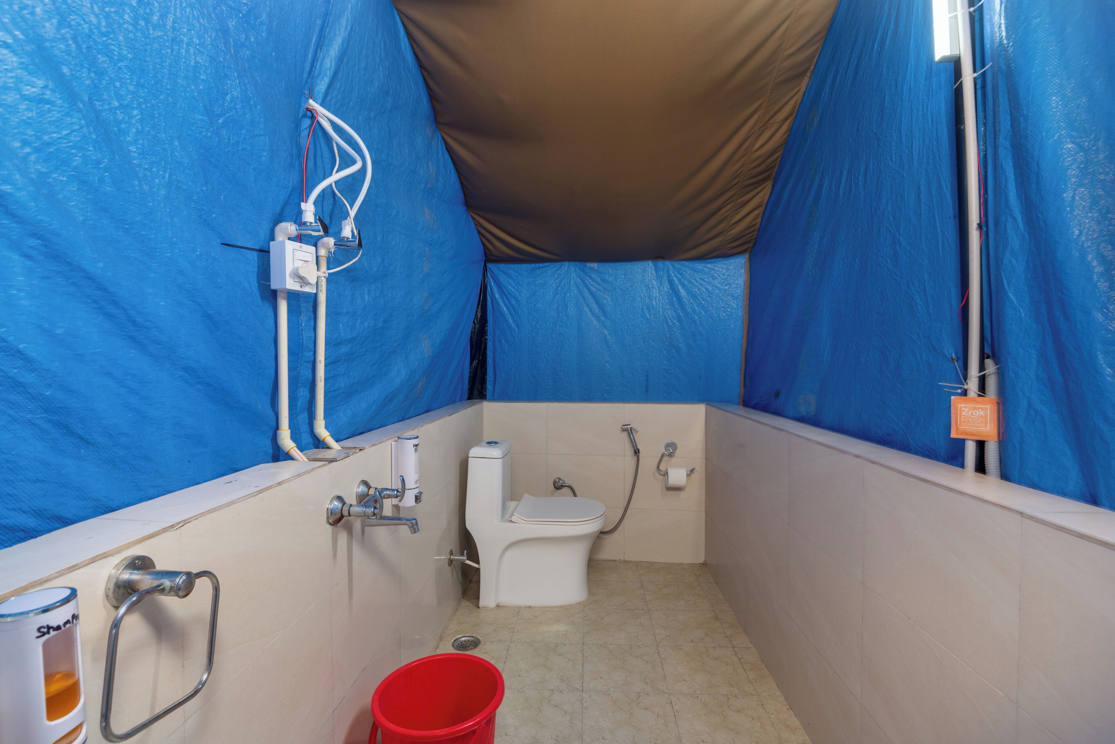 A small, enclosed bathroom with a toilet, shower, and handrails.