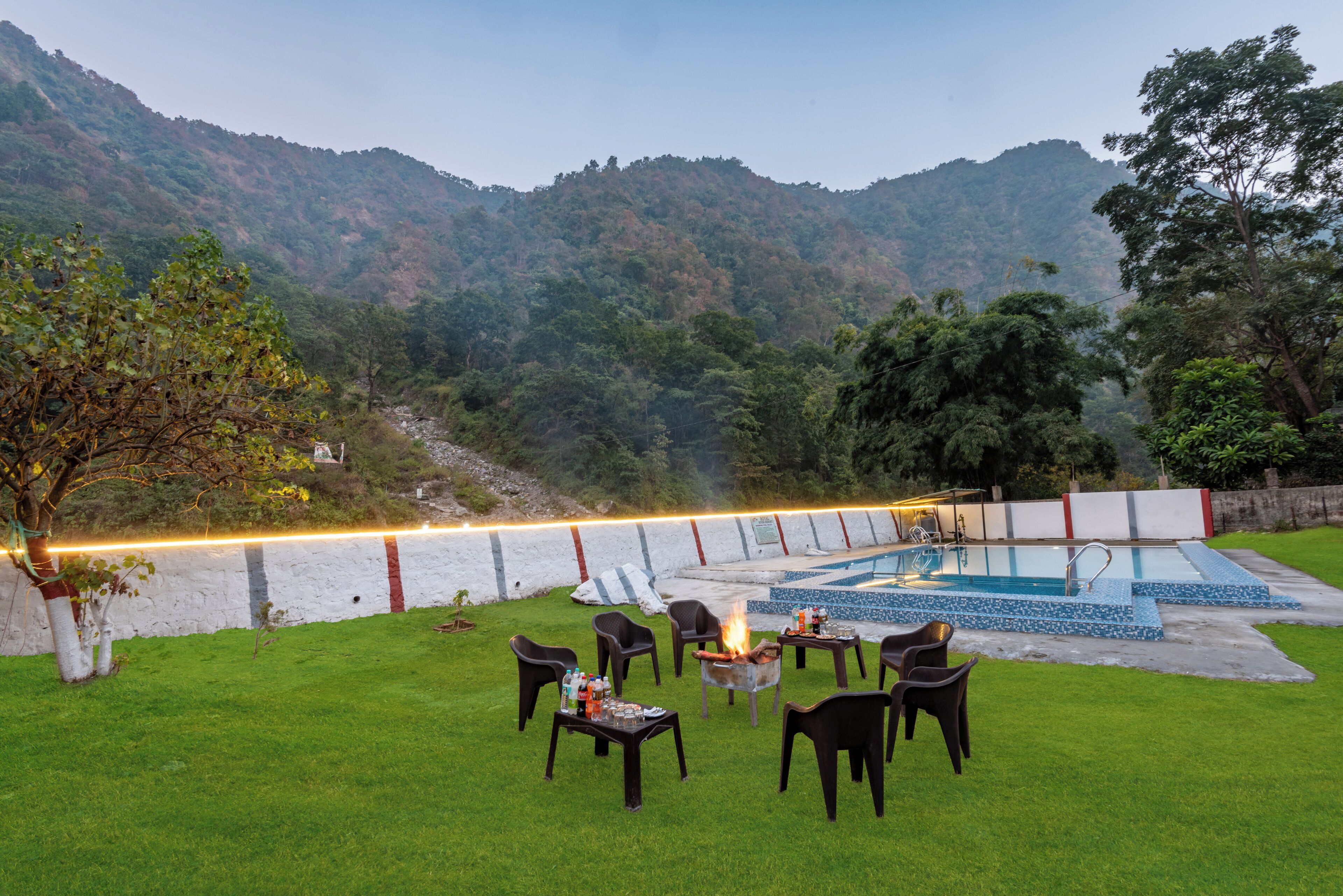 Zona de piscina con sillas y una fogata, rodeada por un muro blanco y vistas a la montaña.