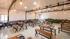 A spacious dining area with multiple wooden tables and benches, a high ceiling with exposed beams, and hanging light fixtures. - River Valley Resort Rishikesh (Rishikesh)