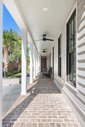 A covered porch with a brick floor, white columns, and a ceiling fan. - Renovated 4bd Prime Location, Victorian Home, Gym (Charleston)