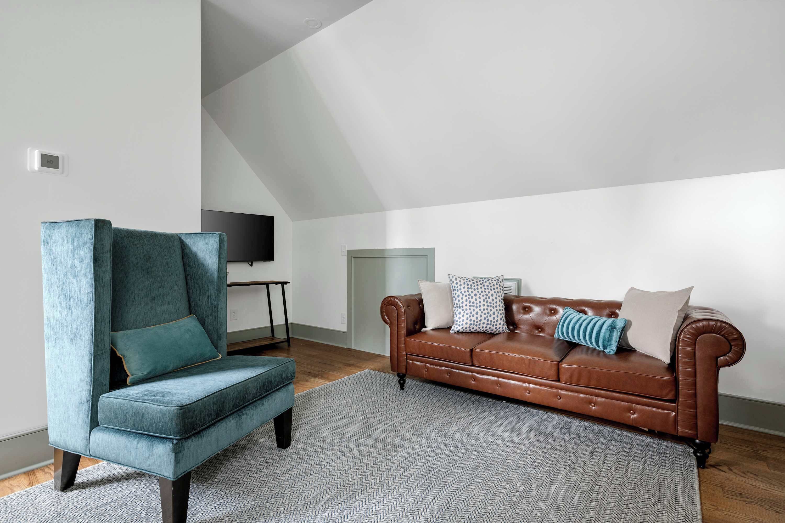 Een moderne woonkamer met een blauwgroene fauteuil, een bruine leren bank en een vloerkleed met een herringbone patroon.
