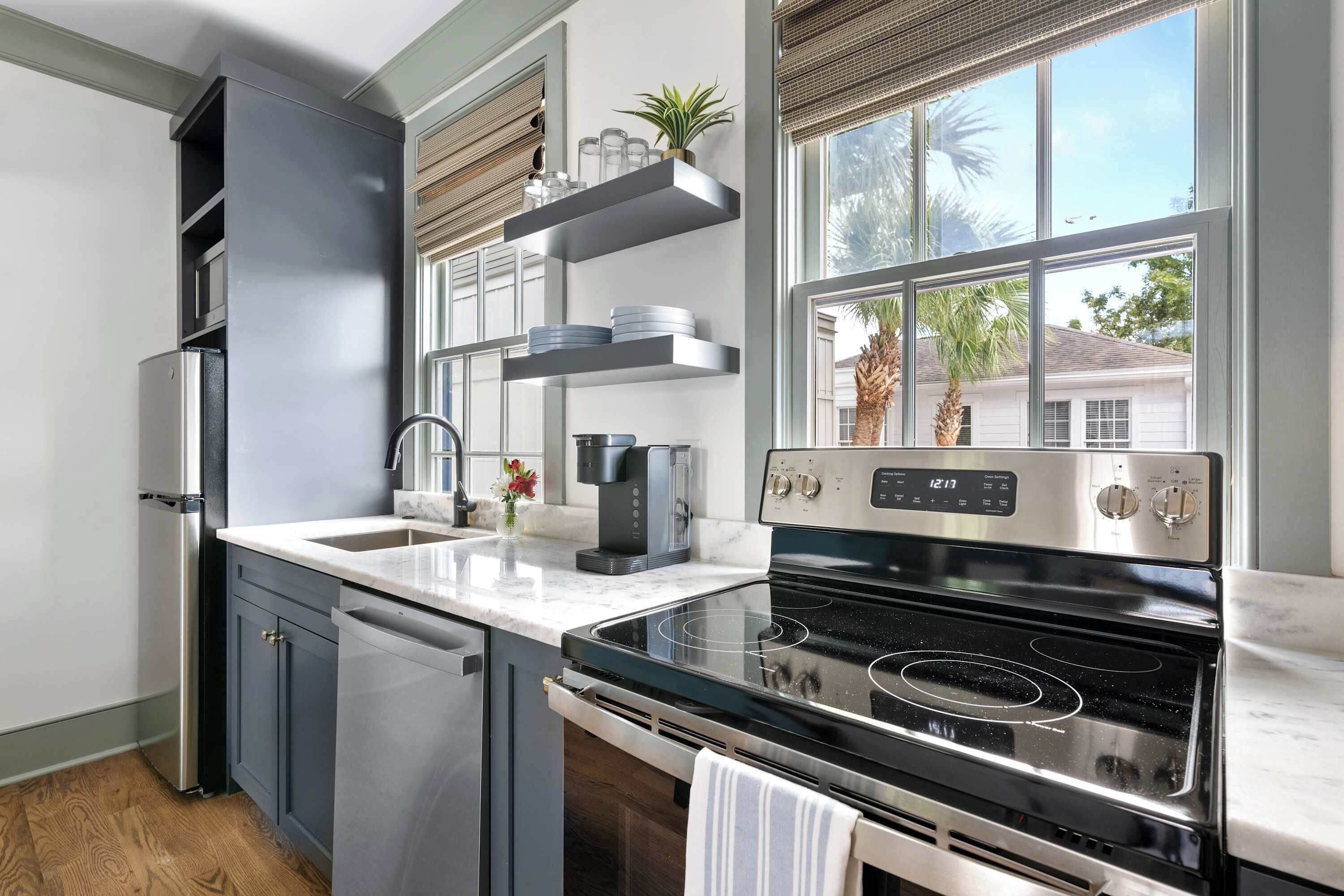 A modern kitchen with a stainless steel stove, built-in oven, and a large window offering a view of palm trees.