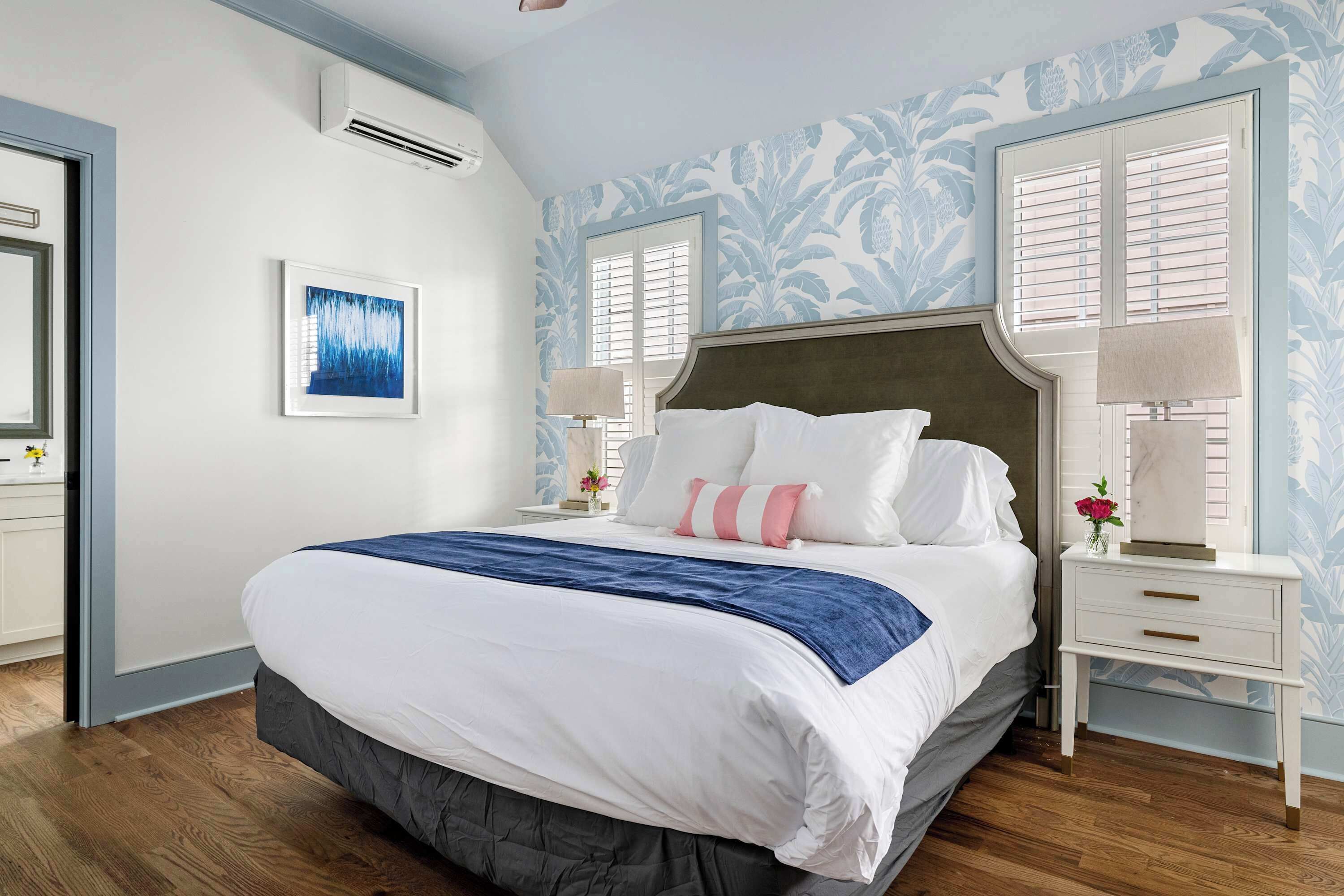 Un dormitorio con una cama grande, paredes blancas y un estampado floral en el papel tapiz.