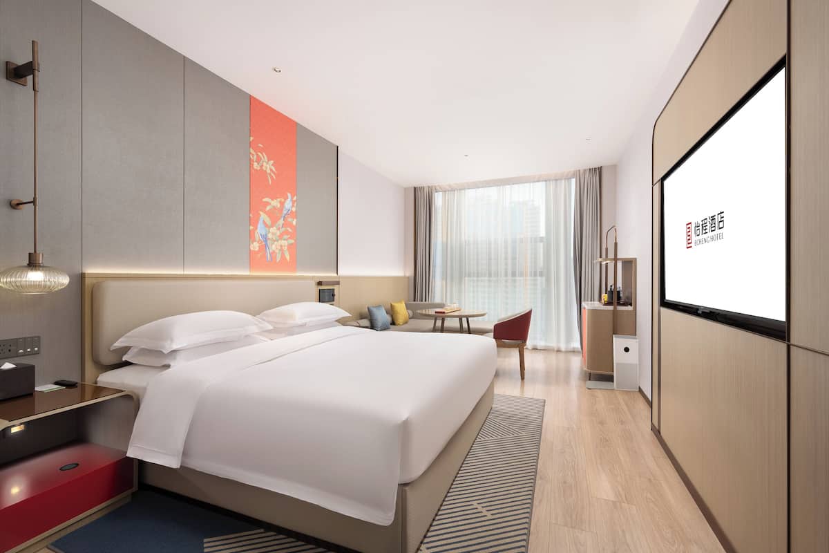 Een moderne hotelkamer met een groot bed, nachtkastje, lamp en een televisiescherm met hotelpromotie.