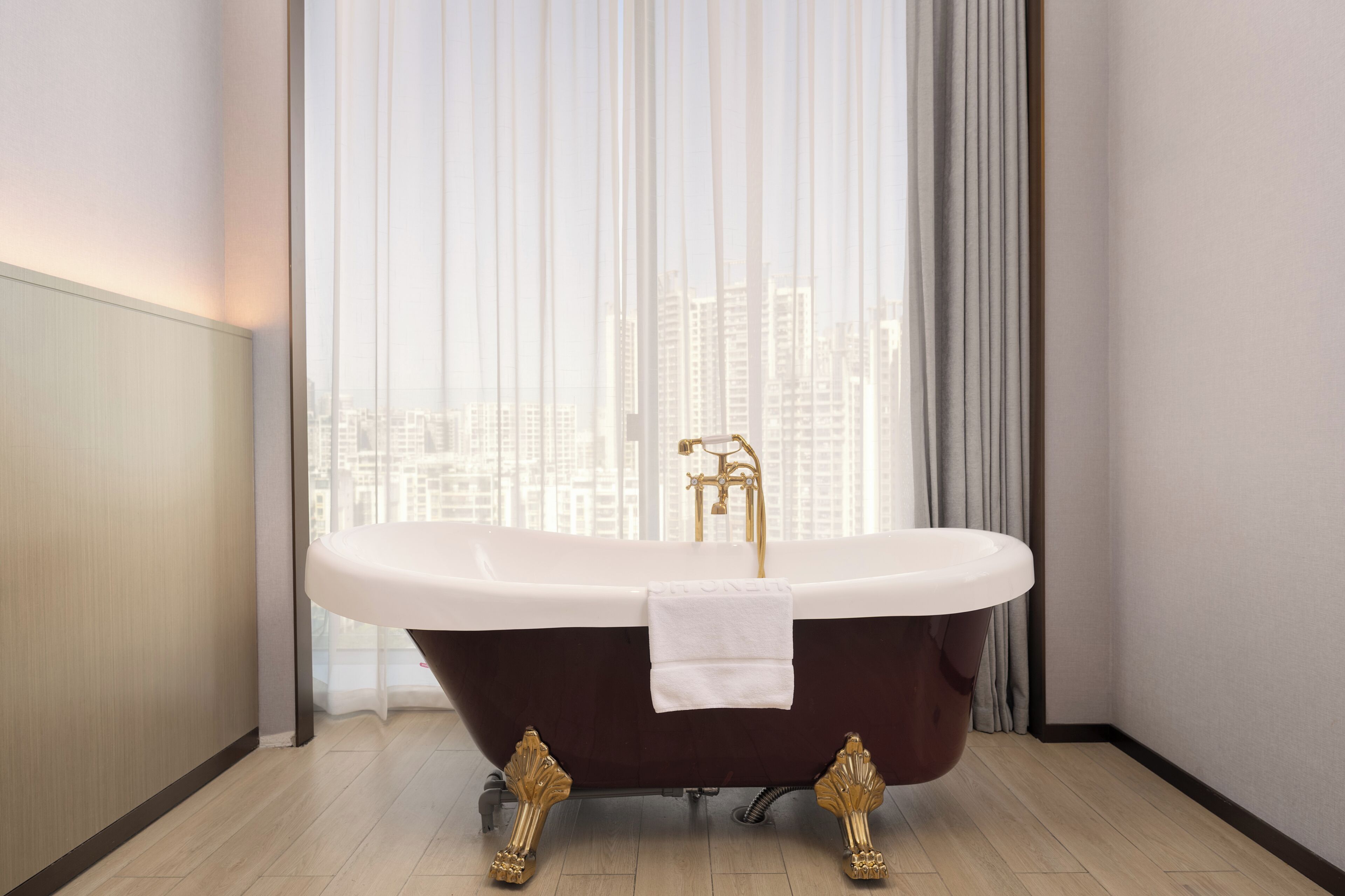 A freestanding bathtub with gold fixtures in a modern bathroom with a city view.