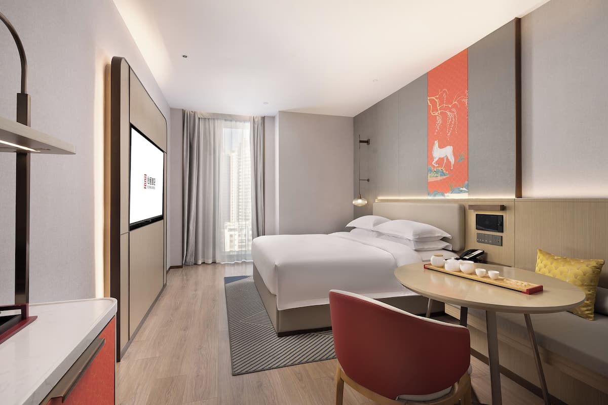 Een moderne hotelkamer met een bed, een bureau, een stoel, een tafel met kopjes en een televisiescherm.