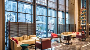 A spacious lobby with a high ceiling, large windows offering a view of tall buildings, a seating area with sofas and chairs, and a bookshelf filled with books. - Nanning Huafengcheng ECHENG Hotel (Nanning)