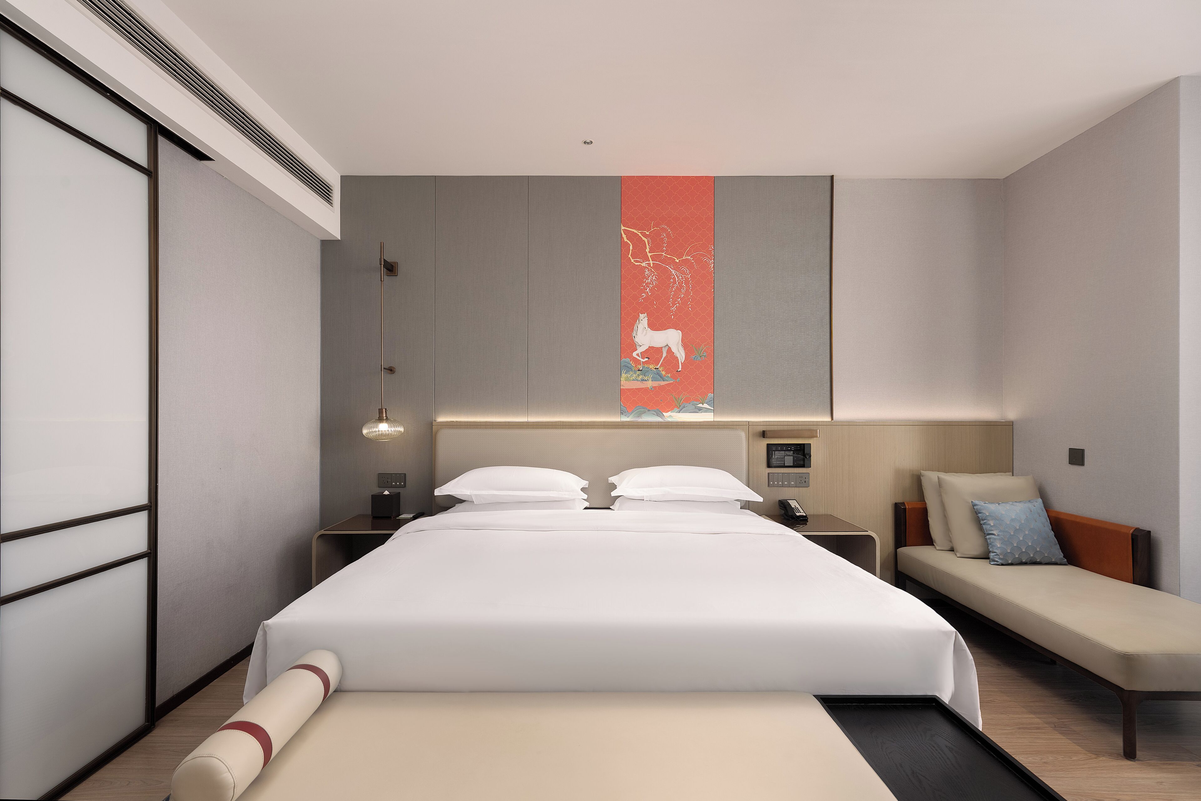 Ein modernes Hotelzimmer mit einem großen Bett, Nachttischen, einer Bank und einem Wandkunstwerk.