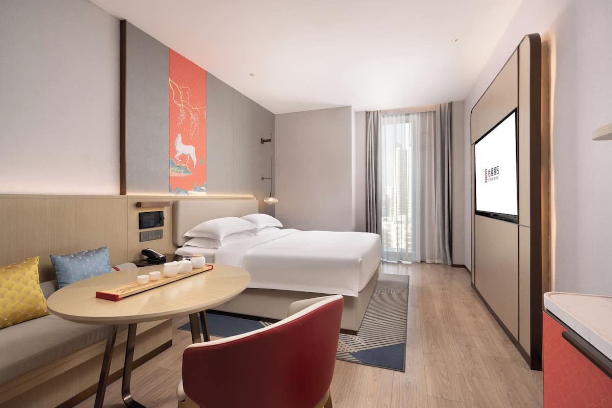 Een hotelkamer met een bed, bureau, stoel, televisie en een raam met gordijnen.