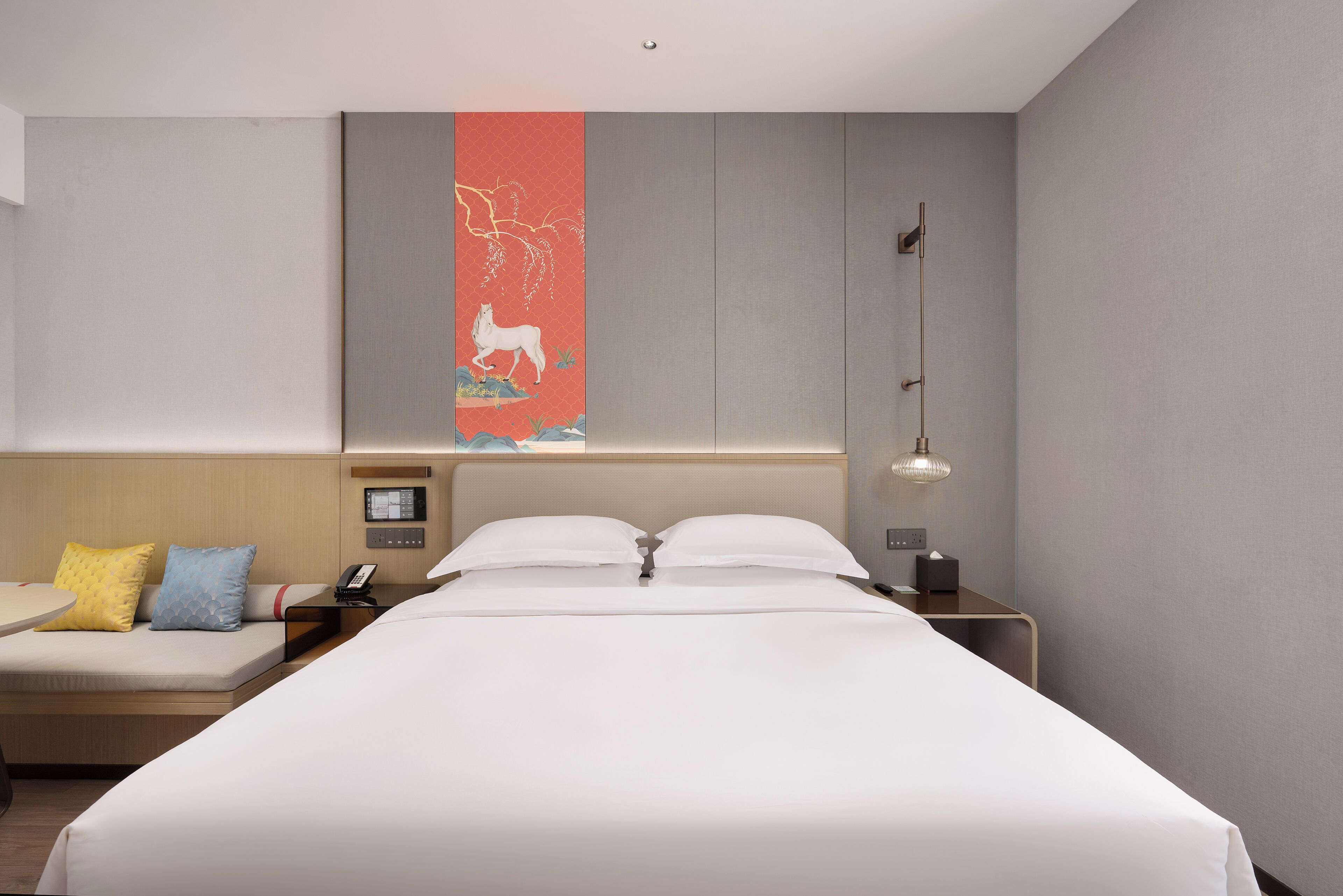 A hotel room with a large bed, a bedside table with a lamp, a phone, and a small table with a chair.