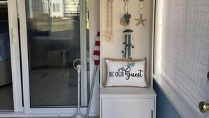 Une pièce dotée d’une porte-fenêtre coulissante donnant sur un patio, d’un meuble blanc agrémenté d’objets décoratifs et d’une pancarte sur laquelle on peut lire : « SOYEZ LES BIENVENUS ».