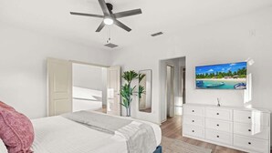 Una camera da letto con un letto, una ventola a soffitto, un televisore a parete e un comò.