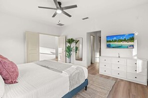 A bedroom with a bed, a ceiling fan, a TV on the wall, and a dresser. - Resort de Tropical - Team Joseph Ellen (Jacksonville Beach)