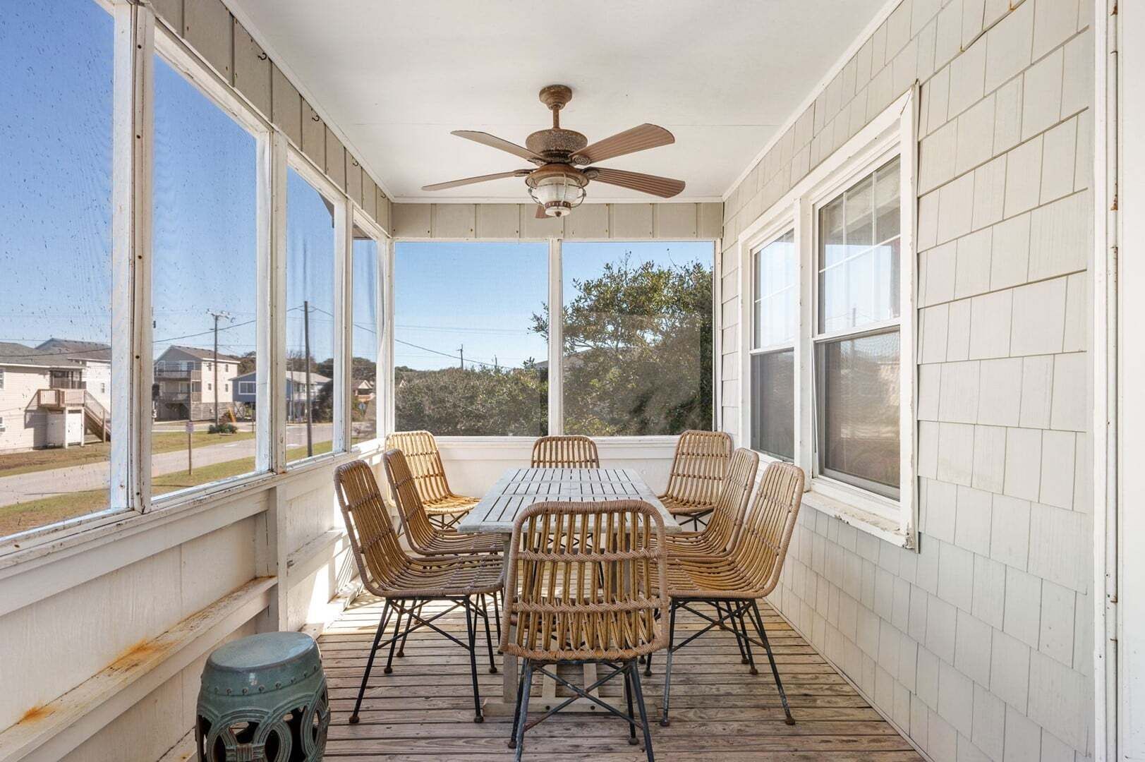 Eine überdachte Veranda mit Tisch und Stühlen, einem Deckenventilator und großen Fenstern.