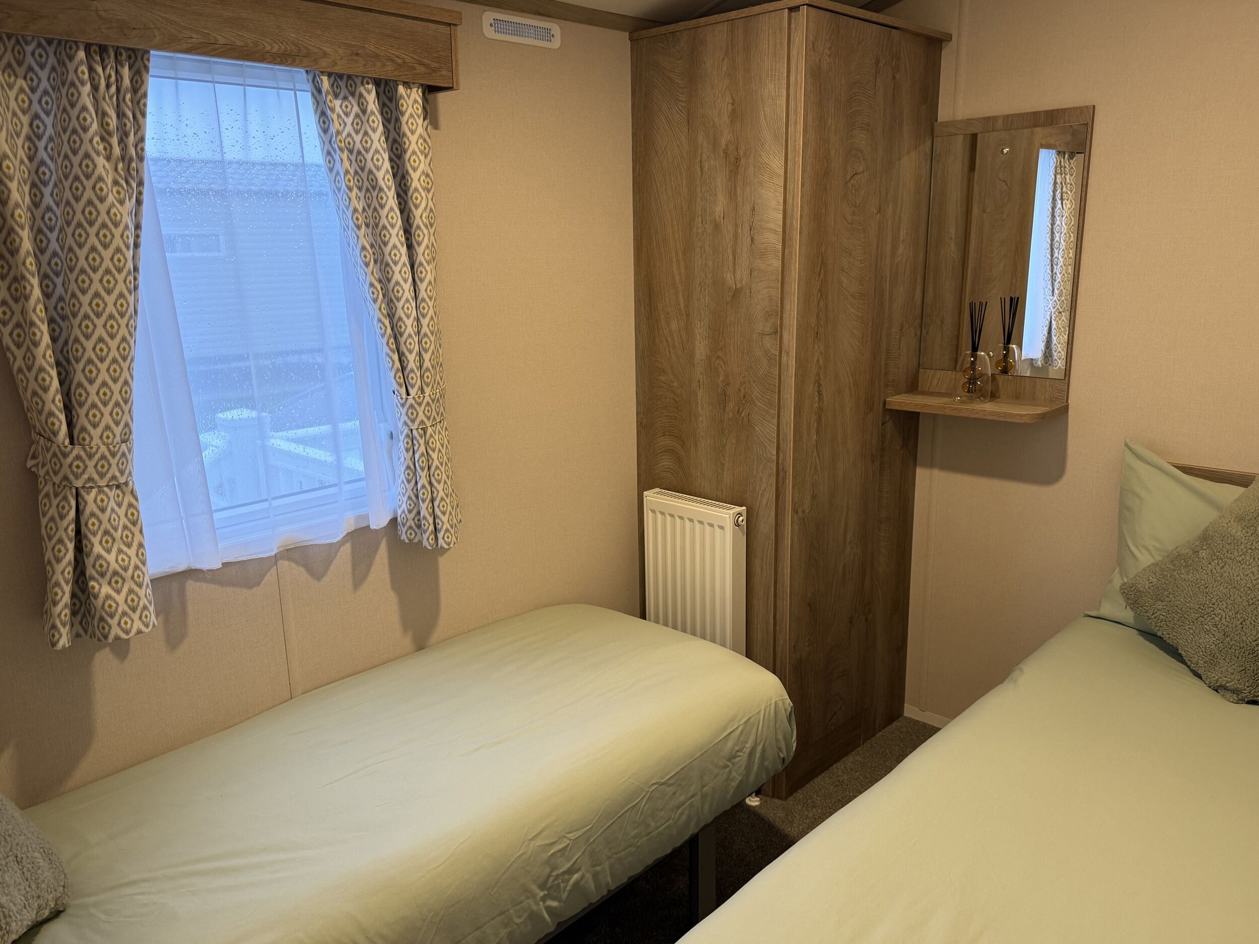 Un dormitorio con dos camas individuales, un armario de madera, un radiador y un espejo en la pared.