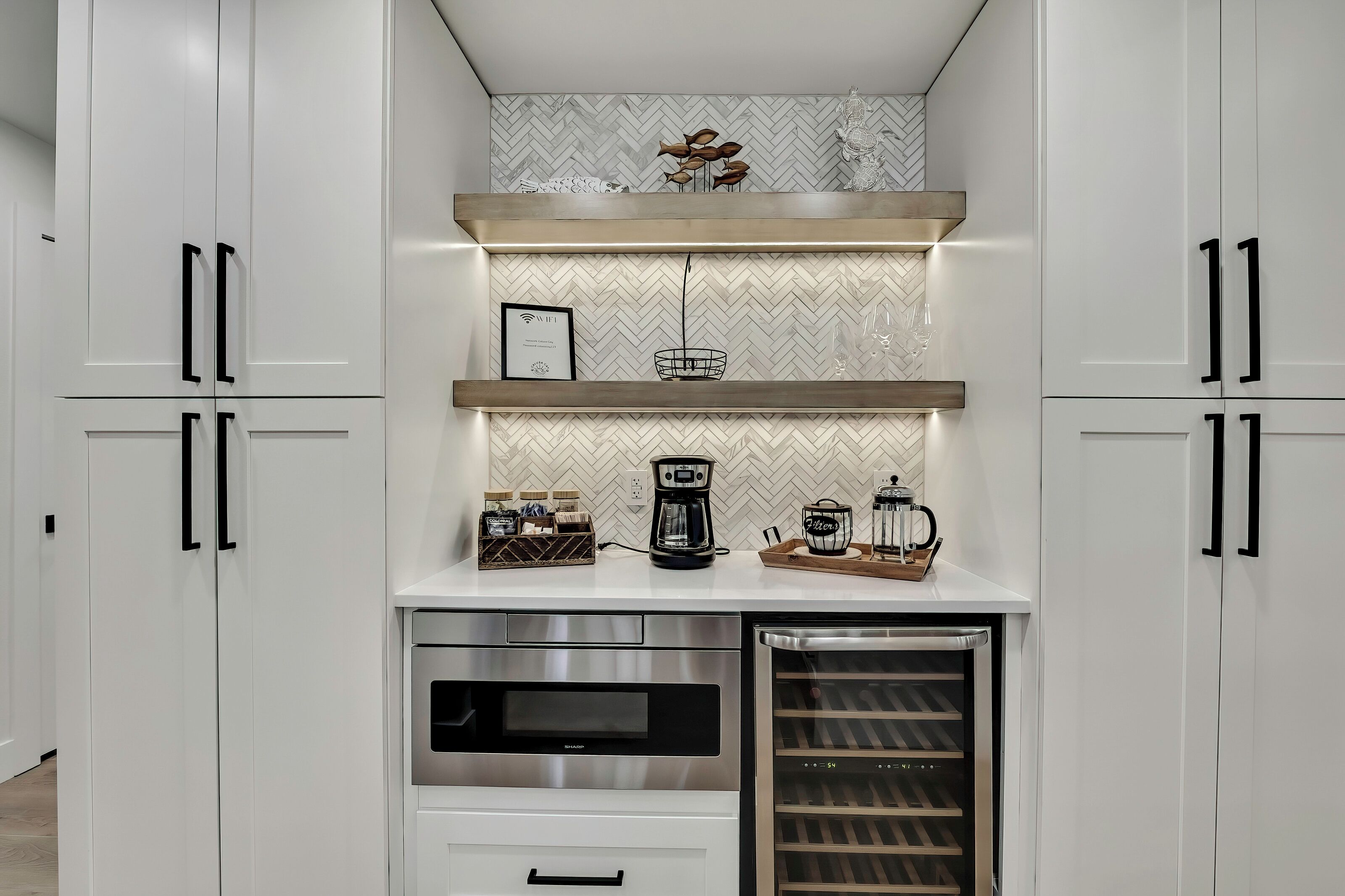 Uma cozinha moderna com armários brancos, um refrigerador para vinhos embutido e um espaço para café.