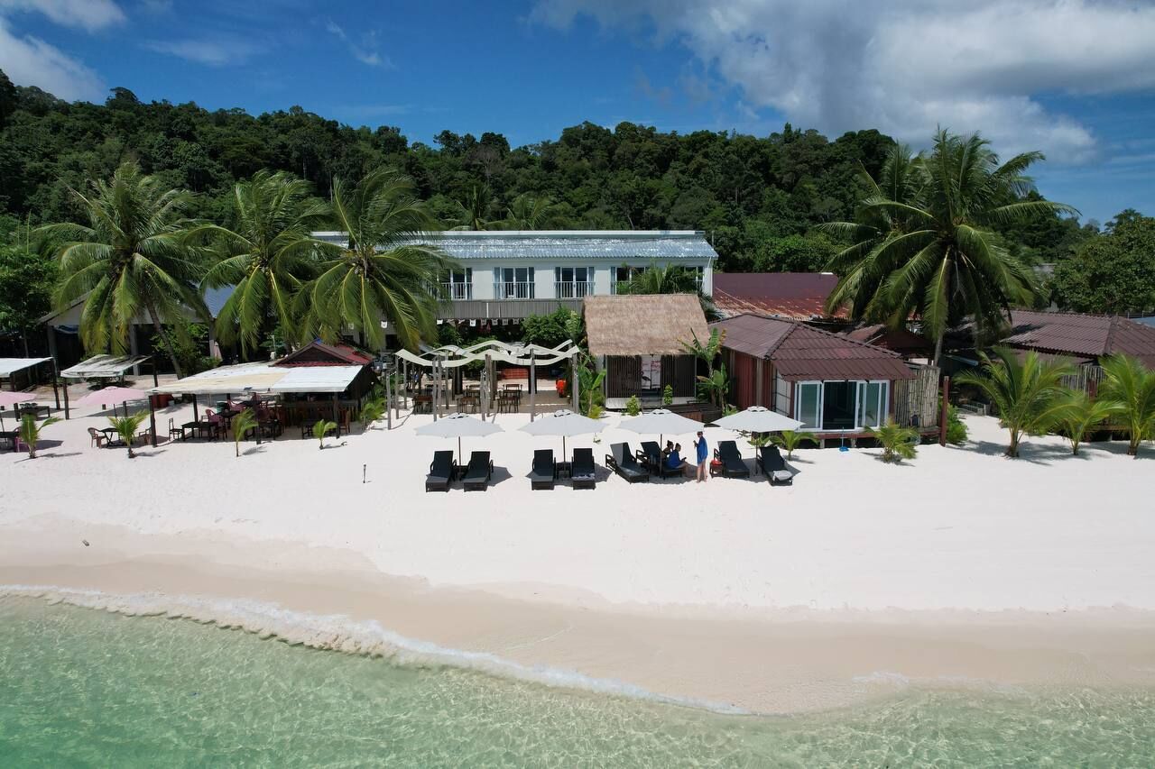 Ein Strandhotel mit Poolbereich, Palmen und einem strohgedeckten Gebäude.