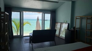 A room with a bed, a chair, a small table, and a view of the ocean through large windows. - White Sand Ark Resort (Koh Rong)
