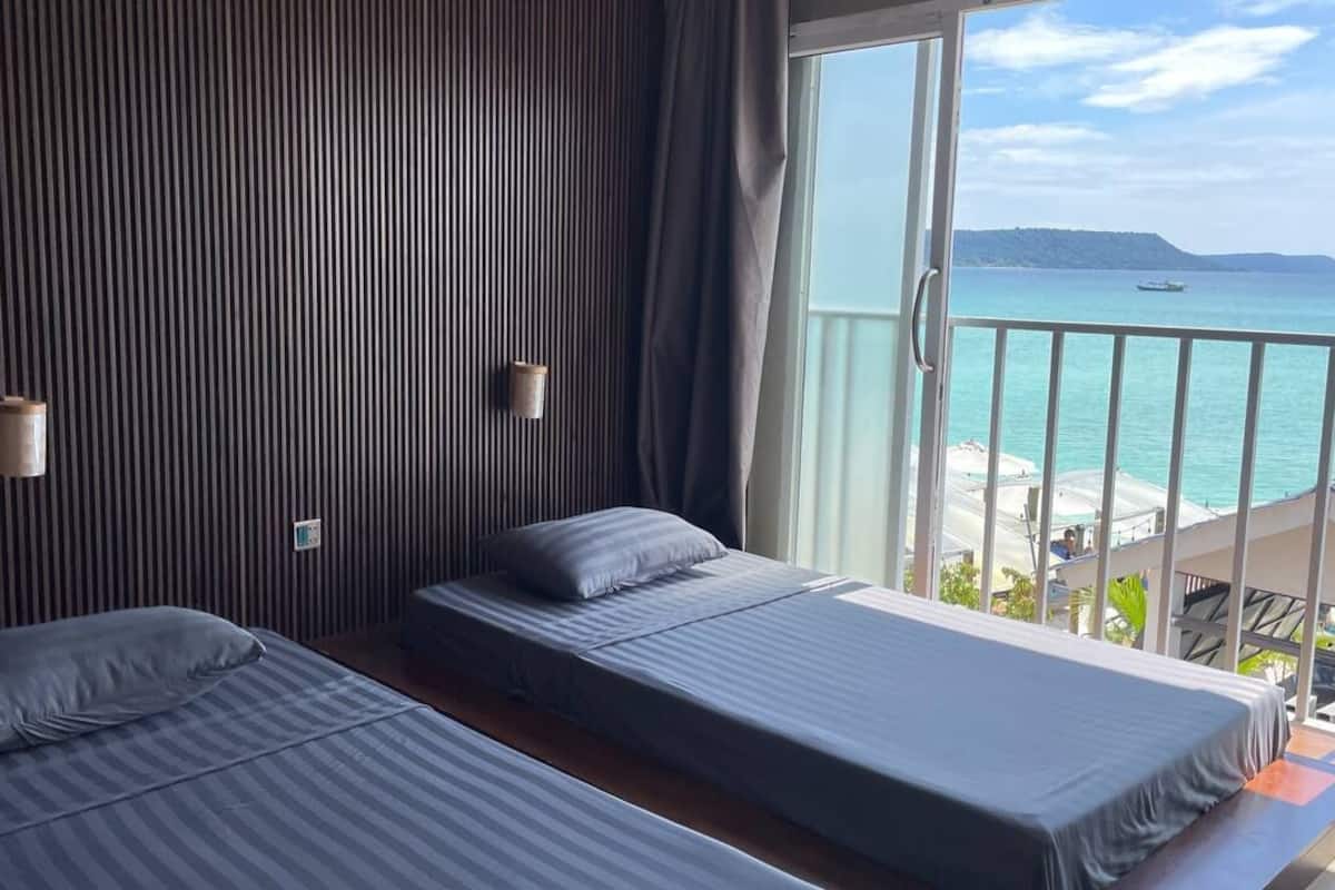Una habitación con dos camas, un ventanal con vistas al mar y un balcón.