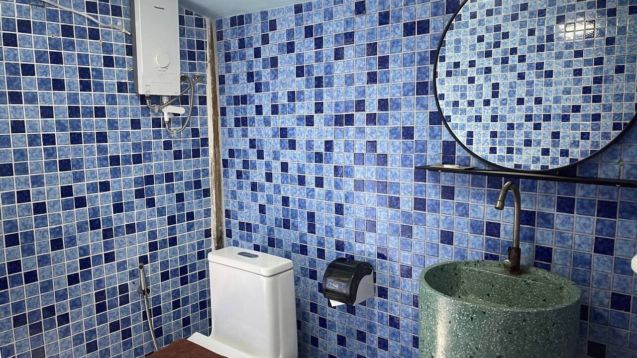 A bathroom with blue mosaic tiles, a white toilet, a round sink, and a mirror.